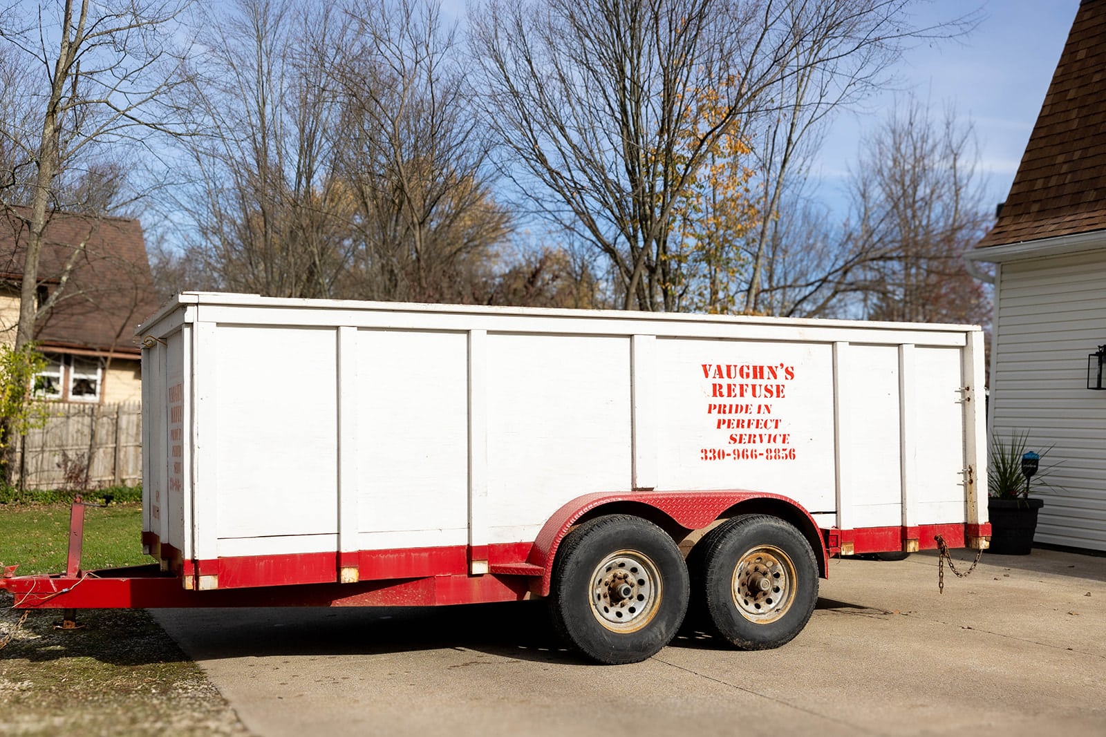 White dumpster trailer labeled 'Vaughn's Refuse' with red text parked outdoors near trees, showcasing reliable dumpster rental services.